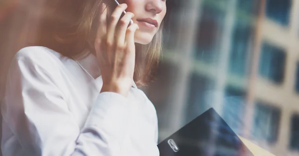 Фото бізнес-леді в сучасному костюмі, розмовляє смартфоном і тримає документи в руках. Відкритий офіс в стилі лофт. Панорамний фон вікон. Горизонтальний макет. Фільм, ефект спалаху — стокове фото