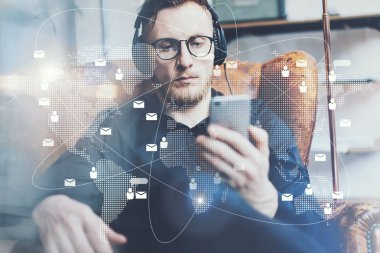 Portre yakışıklı sakallı adam kulaklık müzik dinlerken, video cep telefonu modern loft stüdyo izliyor. Adam akıllı telefon tutan ve rahatlatıcı. Bağlantılar dünya çapında arayüzler. Yatay, film efekti.