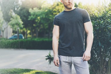 Fotoğraf Sakallı Kaslı Adam Yaz aylarında Siyah Boş t-shirt giyiyor. Green City Garden.Zor iş gününden sonra dinlenme zamanı. Bulanık Arka Plan.Ön görünüm. Yatay Mockup.