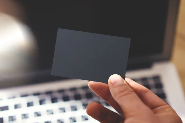 Closeup Photo Man Mostrando cartão de visita preto em branco e usando laptop moderno desfocado fundo. Mockup pronto para informações privadas. Reflexões de luz solar Gadget de superfície. Mock horizontal para cima . — Fotografia de Stock