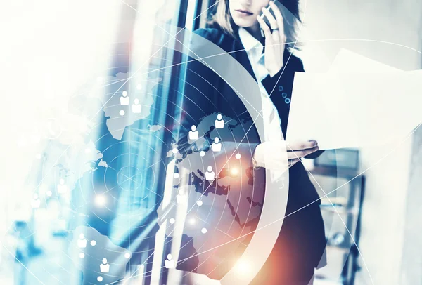 Photo business woman wearing black suit,talking smartphone and holding papers hands.Open studio office.Panoramic windows background.Connections world wide interfaces.Horizontal,flares.Film effect. — Stock Photo, Image