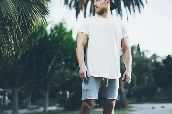 Foto hombre musculoso barbudo que usa una camiseta blanca en blanco en verano. Green City Garden.Tiempo de relajación después del día de trabajo duro. Fondo borroso.Vista frontal.Mockup horizontal . —  Fotos de Stock