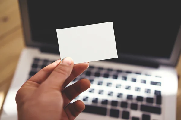 Foto Mann zeigt leere weiße Visitenkarte und mit modernen Laptop unscharfen Hintergrund. Attrappe bereit für private Informationen. Sonnenlicht reflektiert Oberflächen-Gadget. horizontale Attrappe. — Stockfoto