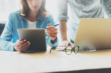 İş arkadaşları modern ofiste beyin fırtınası süreci ekibi. Proje yapımcısı okuma raporu tablet, gözlük ahşap masa. Genç iş ekibi başlangıç stüdyosu ile çalışıyor. Laptop kullanarak. Bulanık, film effec