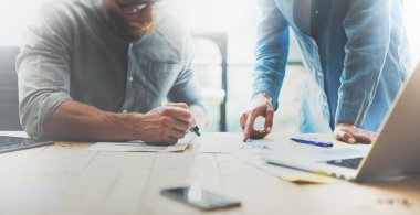 İş arkadaşları modern ofiste beyin fırtınası süreci ekibi. Proje yöneticisi gözlük takıyor, adam nota kalemi yapıyor. Genç iş ekibi başlangıç stüdyosu ile çalışıyor. Dizüstü ahşap masa. Bulanık, film effec