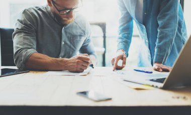İş arkadaşları modern ofiste beyin fırtınası süreci ekibi. Proje yöneticisi gözlük takıyor, adam nota kalemi yapıyor. Genç iş ekibi başlangıç stüdyosu ile çalışıyor. Dizüstü ahşap masa. Bulanık, film effec