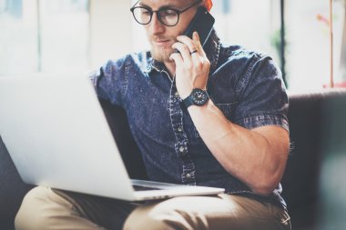 Kas Sakallı Adam çalışma Laptop modern İç Tasarım Loft Ofis, Oturma Vintage Kanepe.Çağdaş Smartphone Hand.Blurred Background.Creative Business Startup Process Idea.Horizontal Film kullanma