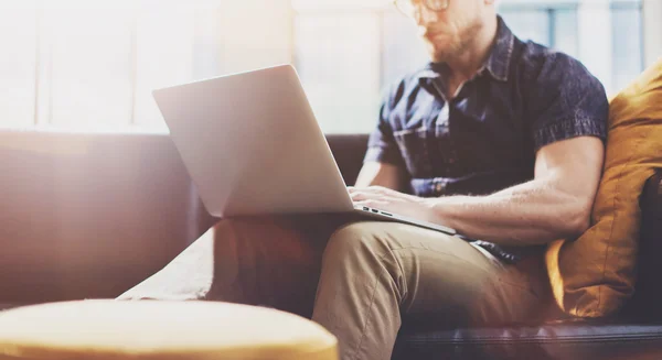 Bearded Hipster working Laptop modern Interior Design Loft Office.Man work Vintage Sofa,Use contemporary Notebook,typing keyboard.Blurred Background.Creative Process Business Startup Idea.Horizontal.