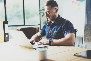 Sakallı grafik tasarımcı çalışma ahşap masa dizüstü Modern İç Tasarım Loft Office.Man İş Coworking Studio.Use çağdaş Notebook, klavye yazarak. Bulanık Arka Plan.Creative Business Startup.