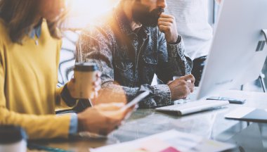 Business Startup Concept.Coworkers Teamworking Process.Bearded Hipster Typing Modern Computer.Young Woman Using Smartphone Hands.Creative People Work New Project Wood Desk Table.Blurred Flares Etkisi.