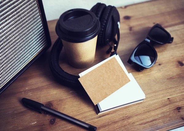 Closeup yığın boş Kraft kağıt kartvizit Mockup ahşap masa Background.Take uzak kahve fincanı Coworking Studio.Modern kulaklık taşınabilir hoparlör güneş gözlüğü iç Cafe.Lifestyle Mock nesneleri. — Stok fotoğraf