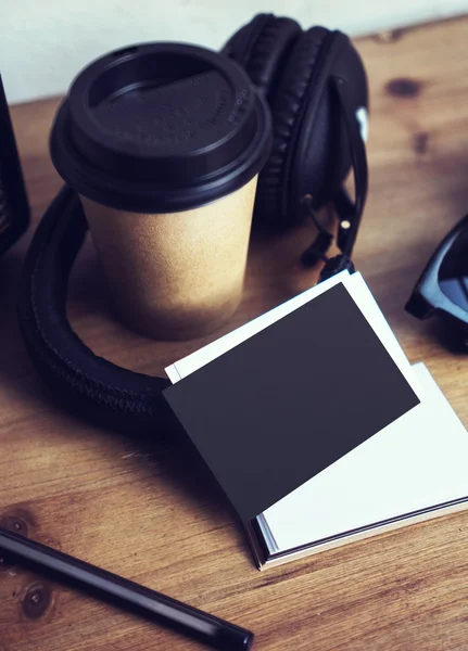 Close-up stack leeg papier visitekaartje mockup hout tabel. Kraft take away koffie kopje Coworking Studio. moderne koptelefoon draagbare zonnebril interieur Cafe achtergrond. verticaal mock up-objecten. — Stockfoto