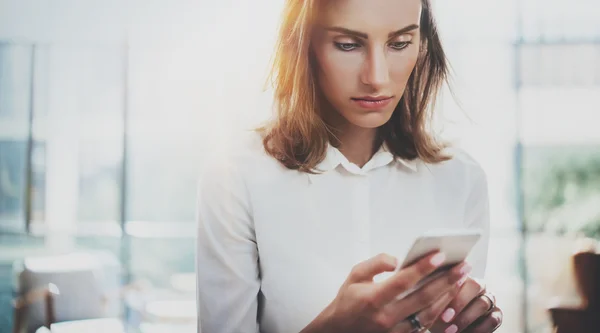 Portret jonge zakenvrouw wit overhemd met behulp van moderne smartphone handen dragen. Meisje SMS sms bericht werkproces. Zonnige ruimte loft kantoor. Panoramische ramen achtergrond. Horizontale wazig. — Stockfoto