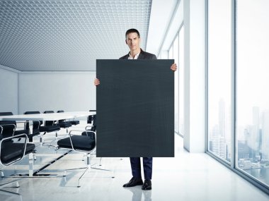 Businessman holding blank blackboard at office clipart