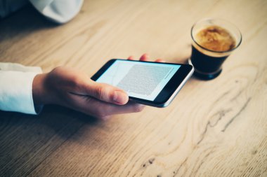 Smartphone tutan kadının el. Masada kahve fincan