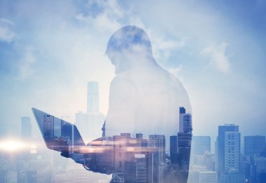 Double exposure of man with laptop and contemporary city on the background