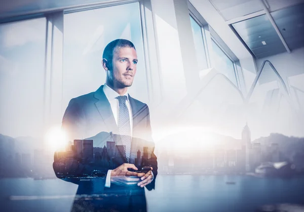 Double exposure of city and businessman using his smartphone — Stock Photo, Image