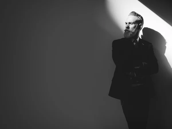 Stylish bearded man wearing trendy suit, stands against a wall  and looking on  left side of the frame — 图库照片