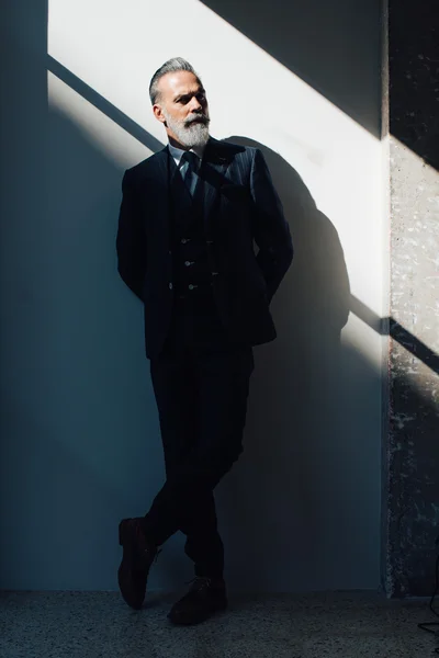 Elegante hombre barbudo con traje de moda y de pie contra la pared —  Fotos de Stock