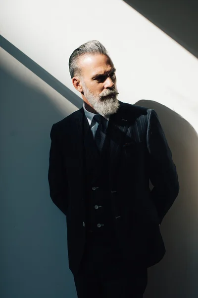 Retrato de homem barbudo vestindo terno da moda e fica contra a parede — Fotografia de Stock