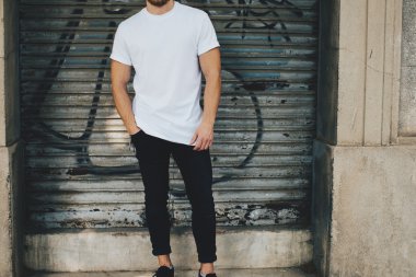 Sakallı adam beyaz boş t-shirt ve garaj duran siyah kot giymiş