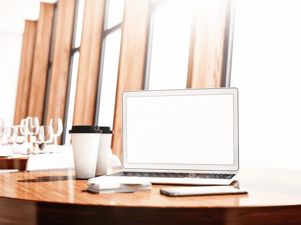 Laptop im generischen Design, Visitenkarten, Smartphone und leere Kaffeetassen auf dem Tisch im modernen Restaurant-Interieur. 3D-Darstellung — Stockfoto