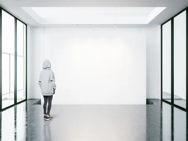 Mujer joven en galería moderna vacía mirando el lienzo en blanco . — Foto de Stock