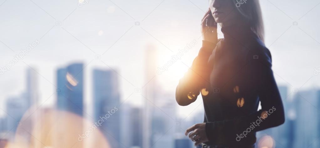 Portrait of young woman holding her smartphone in a hands. Blurred city on the background. Wide