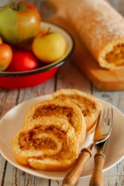 Freshly baked, apple pastry roll dusted with powdered sugar, displayed on a rustic wooden board.