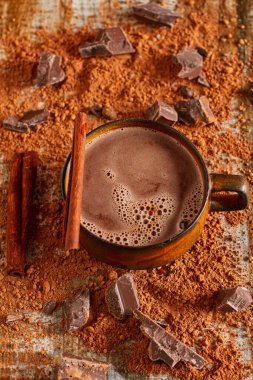 Kakao tozu, kahve çekirdekleri ve tarçın çubuklarıyla kaplı zengin, çikolatalı sıcak içeceklerle dolu bir fincanın fotoğrafı..