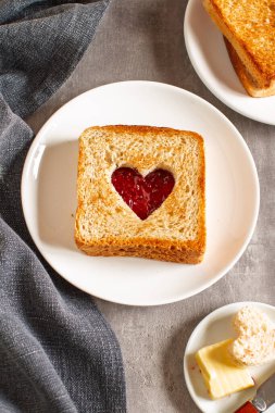 Beyaz tabakta çilek reçeli dolu kalp kesikli tost, romantik kahvaltı konsepti.