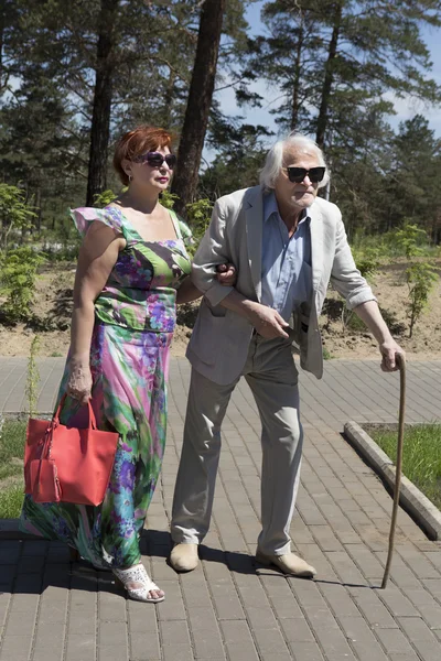 Um homem idoso com dor nas costas caminha com sua esposa — Fotografia de Stock