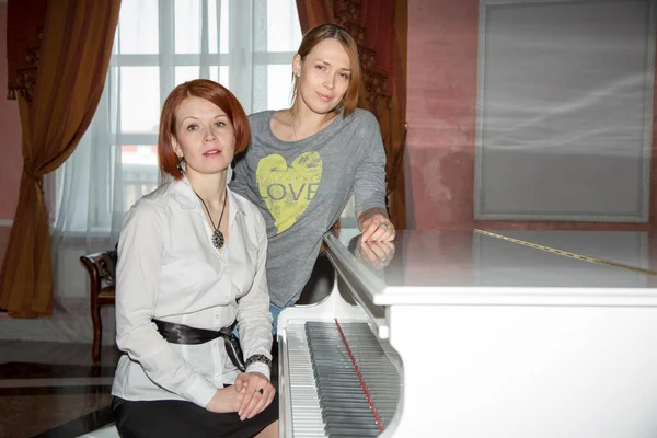 两个漂亮的俄罗斯女人在一架白色钢琴前肖像画 — 图库照片