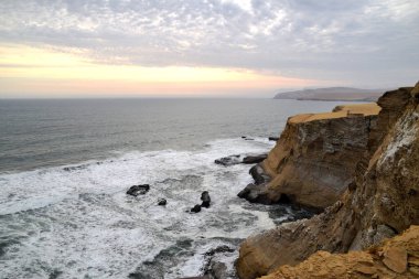 Gün batımında dalgaların gelip kayalara çarptığı güzel bir kıyı manzarası. Peru 'daki Paracas Ulusal Rezervi' nde Pasifik Okyanusu 'nun yanında dramatik uçurumlar.