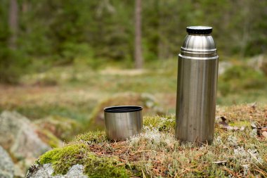 Çelik bir termos ve ormanda yosunların üzerinde duran kahve fincanı. Doğada kahve molası zamanı. Fotoğraf İsveç 'te çekildi..