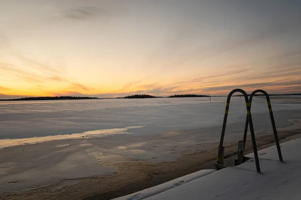 Empty dock ladder for winter swimming in the frozen lake this morning during sunrise. Lake covered in snow and ice. Photo taken in Vasteras, Sweden.