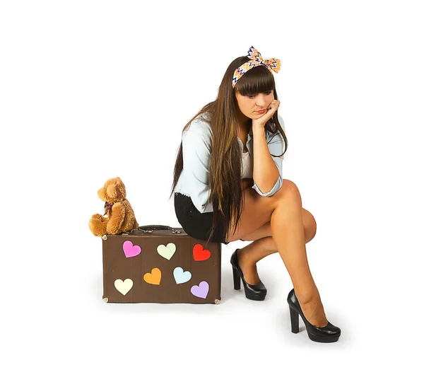 Sad young woman sitting on a suitcase with a teddy bear — Stock Photo, Image