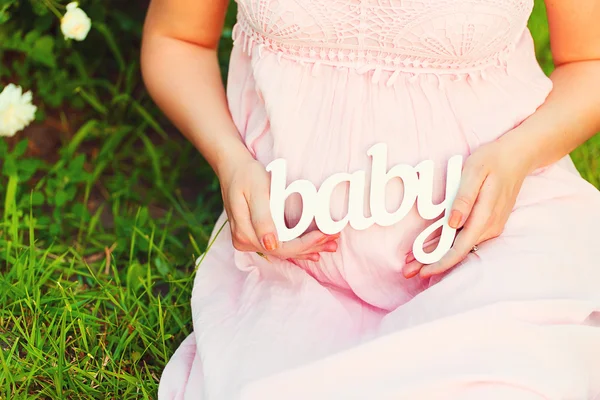 Etikett "Baby" in den Händen einer schwangeren Frau — Stockfoto