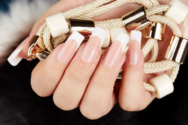 Hand with long artificial french manicured nails holding a necklace