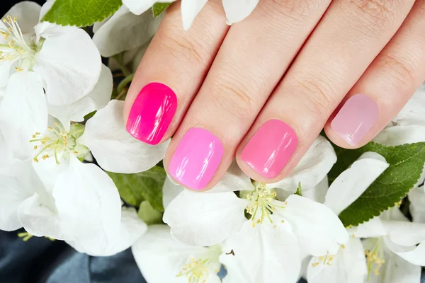 Ręka z manicure paznokcie na tle białych kwiatów — Zdjęcie stockowe