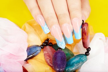 Uzun, yapay, manikürlü tırnaklarıyla bir kolye tutan bir el.