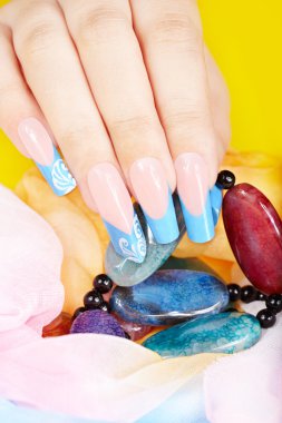 Uzun, yapay, manikürlü tırnaklarıyla bir kolye tutan bir el.