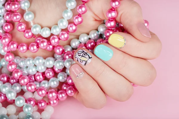 Ruka s krásné pěstěné nehty drží barevné náhrdelníky — Stock fotografie