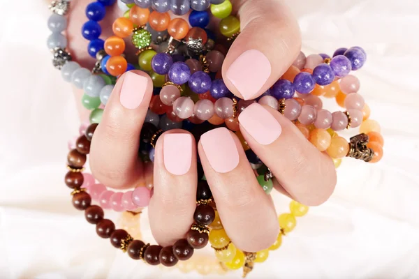 Hand with beige matte manicured nails and colorful bracelets — Stock Photo, Image