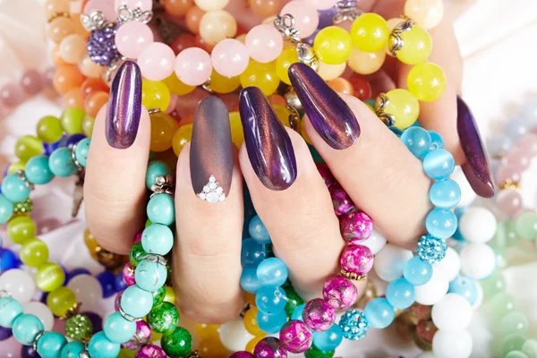 Hand with long artificial manicured nails holding colorful bracelets — Stock Photo, Image