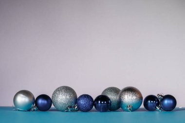 Mavi, beyaz ve gümüş renkli Noel topları turkuaz ve pembe arka planda sıralanır..