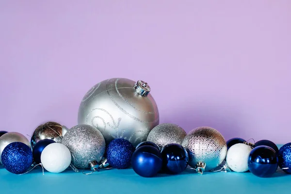 Palle di Natale nei colori blu, bianco e argento sono disposti in fila su uno sfondo turchese e rosa. — Foto Stock