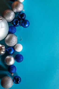 Mavi, beyaz ve gümüş renkli parlak Noel topları, metin için bir boşluk ile turkuaz arka planda sıralanır.