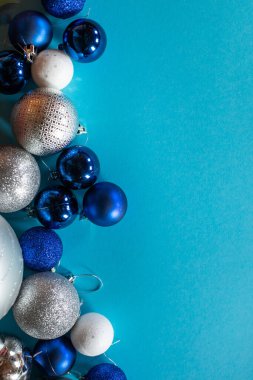 Mavi, beyaz ve gümüş renkli parlak Noel topları, metin için bir boşluk ile turkuaz arka planda sıralanır.