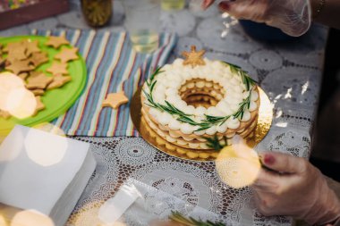 Noel çelengi şeklinde bir Noel pastası. Kadın pasta şefinin elleri, yeni yılın yenilebilir dekoruyla bir pasta süslüyor. Çalışma ortamı..